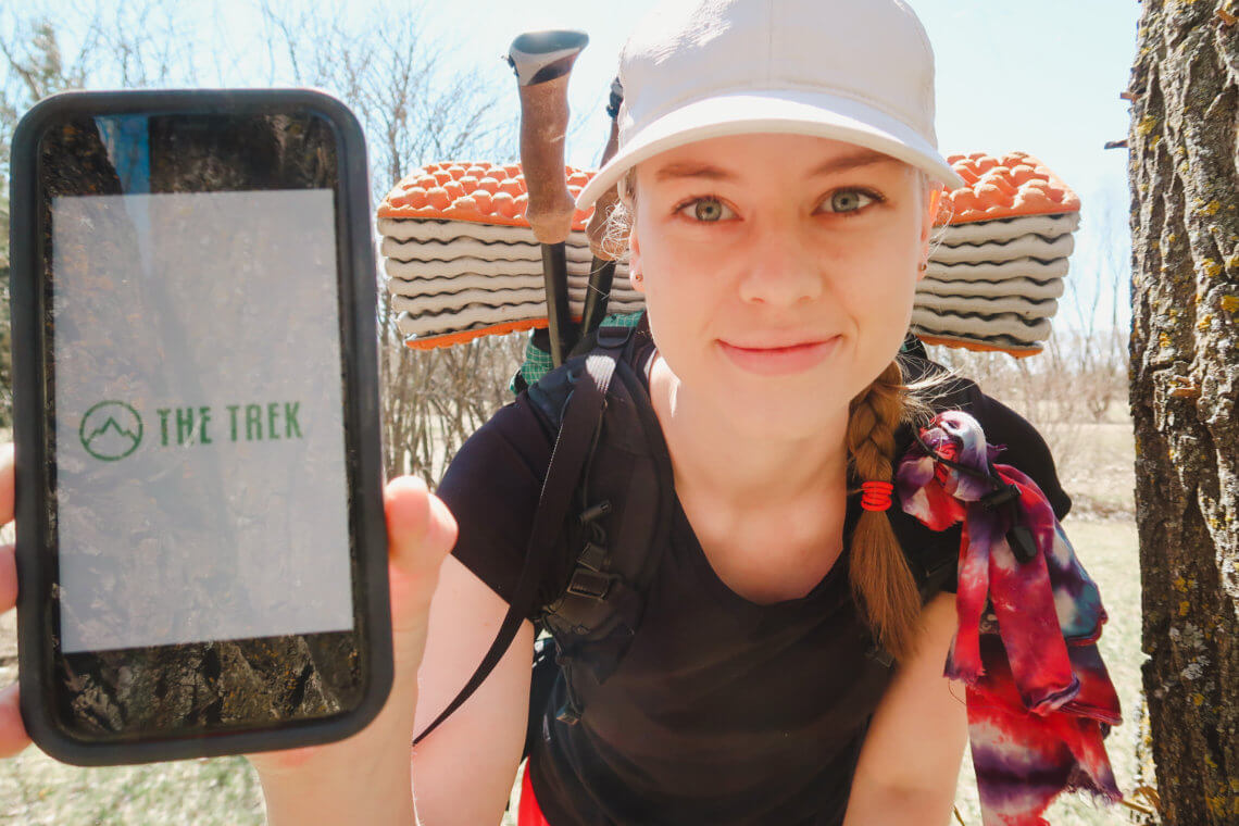 the trek logo appears on phone screen that is held up by a girl in thruhiking gear